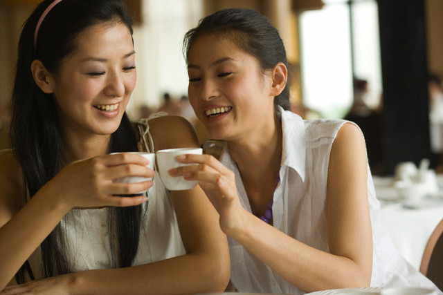 Two young women toasting with tea cups in a restaurant and smiling