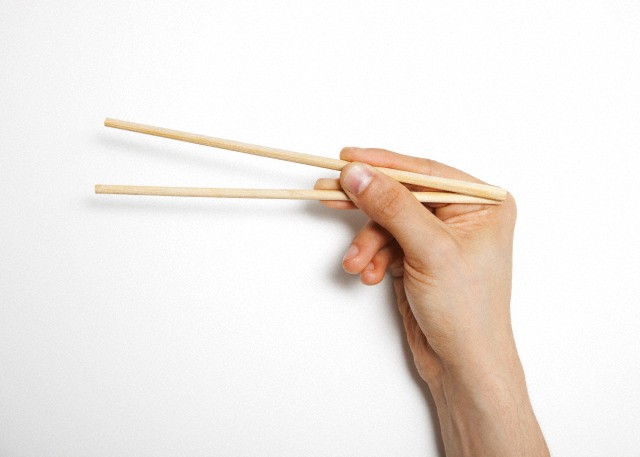 Man's hand gripping chopsticks over white background